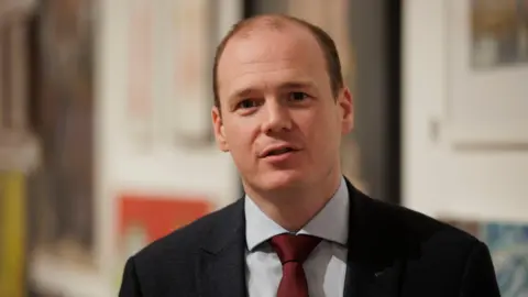 PA Media Lyons is outside. He's wearing a suit with a white shirt and a red tie.
