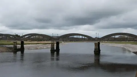 Billy McCrorie/Geograph Jembatan beton yang terbentang di seberang sungai dengan tepian berlumpur yang terlihat