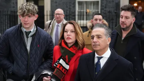 PA Media The families of the Nottingham attacks victims outside No 10 Downing Street. Charlie Webber is wearing a navy quilted jacket, standing next to Emma Webber wearing a red coat and Sanjoy Kumar wearing a tailored wool coat. They are standing in front of Ian Coates's sons James and Lee.  