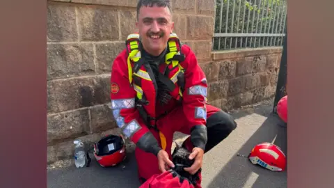 West Yorkshire Fire and Rescue Service A fireman holding a black cat in red a bag
