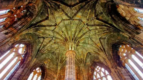 the vaulted roof of a church with arched windows and columns, lit up in reddy brown and a greenish hue