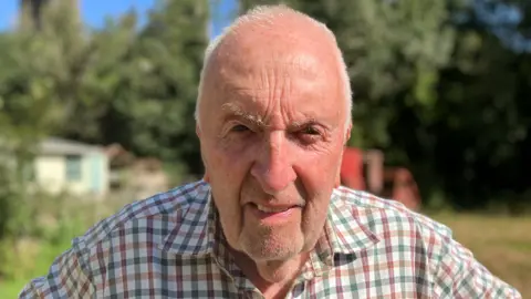 A close-up of John Hosking senior stood in a field looking to camera