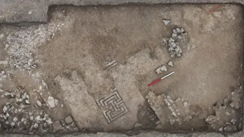 Teffont Archaeology Drone shot of a partially uncovered Roman mosaic floor, mostly monochrome in colour with motifs in square shapes.