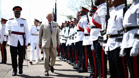 Reuters King Charles III wearing a beige suit with military medals, walks past a long row of Royal Bermuda Regiment troops