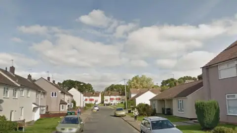 A residential street with houses and bungalows, and some cars parked on the pavement.