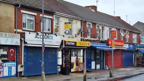 Image shows a branch off Premier Off License on Manchester Street, Swindon, amongst a row of other shops. 