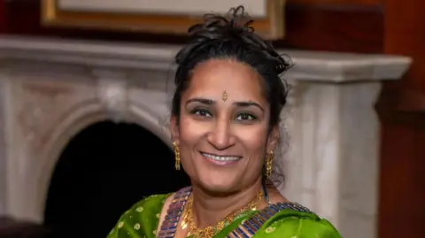 Manjinder Nagra A woman wearing a green sari while smiling at the camera