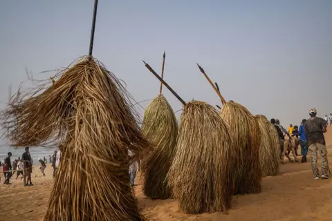 NICOLAS REMENE / AFP People covered in long straw costumes dance in unison.