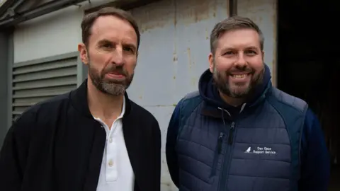 Sam Palmer/BBC Gareth Southgate is posing for a photo with another man who is smiling. Both men have short brown hair and beards.