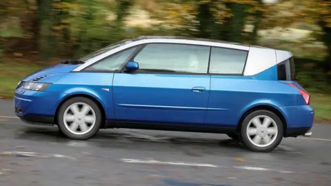 Simon Farmer. Un Renault Avantime azul y plateado circulando por una carretera. Al fondo se ven árboles.