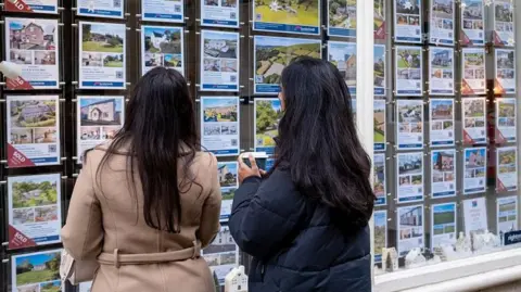 Two women looking at property details in an estate agent's window