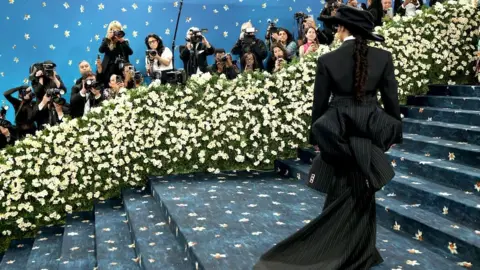 A woman dressed in black stands on the red carpet at the Met Gala in New York. Her back is to the camera, obscuring her identity.