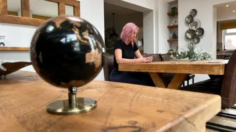Samantha sat in her home in the background, looking at her phone, with a black globe in the foreground.