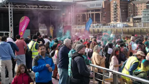 Hundreds are covered in front of a stage as pink and blue paint flies in the air.