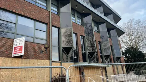 The prospective site of a new Lidl in Woking, Surrey. The derelict building has silver fencing outside and has a 'to let' sign erected to the wall.