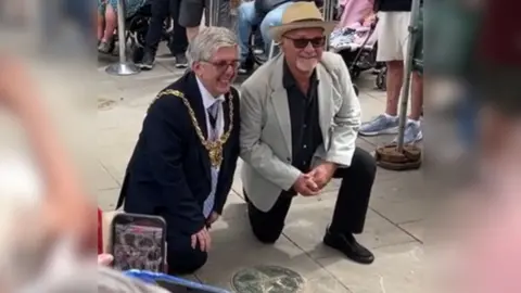 Two men kneeling on the ground beside a metal star in the pavement.
