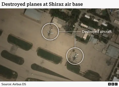 A satellite image showing damage to aircraft at Shiraz air base. The photo shows two destroyed planes sitting on the runway.