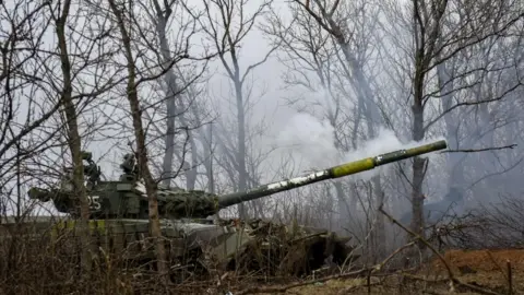 Ukrainian soldiers in a T-72 tank fire on positions in the Donetsk region of eastern Ukraine. There are trees around the tank and smoke is coming out of the barrel