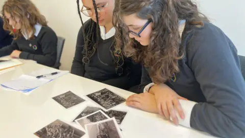 Jon Wright/BBC School students sat at a desk looking at black and white photographs.