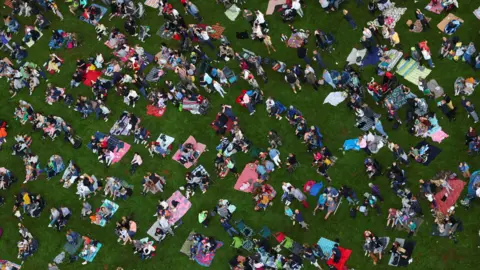 Reuters A bird's eye shot of a crowd sat on the grass at Bristol Balloon Fiesta. Many of them are sat on picnic blankets.