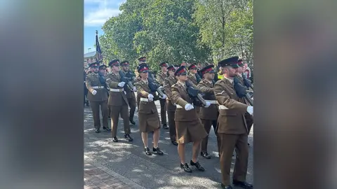 The Duke of Lancaster Regiment at a military parade on a clear day. Trees above the parade and a church spire in the distance.