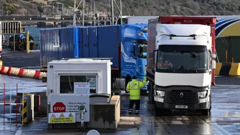 Getty Images Goods vehicles are checked as they arrive at the port of Larne harbour.  A person in a high-vis jacket speaking to the driver of a lorry.