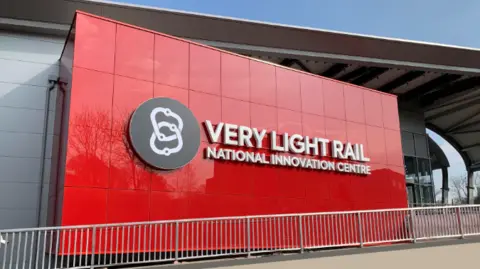 A large red panelled sign on the side of a grey building reads "Very Light Rail National Innovation Centre" in white lettering.