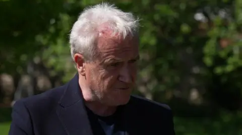 A grey-haired man wearing a dark blue suit jacket