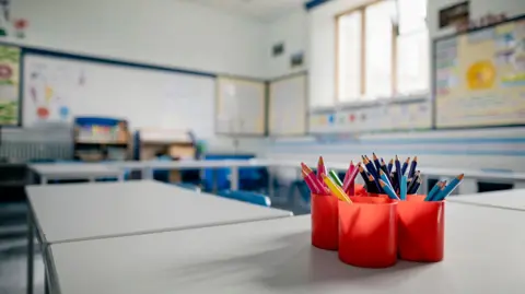 A classroom with four red cups on a table, each filled with colouring pencils. 