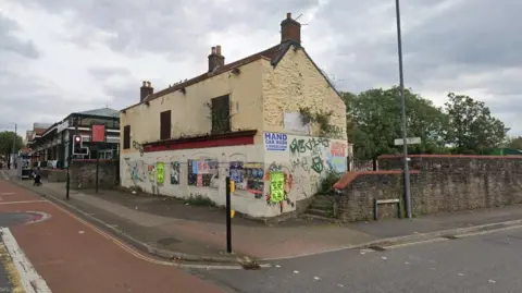 An empty, derelict looking building on the corner of a street. It is covered in posters and graffiti