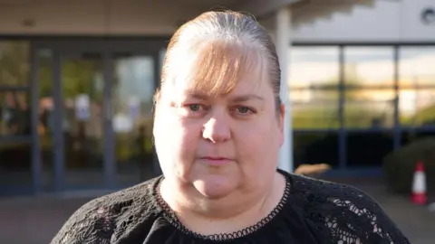 Qays Najm/BBC A woman with light hair wearing a black top in front of Suffolk Coroner's Court.