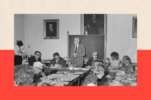 Getty Images Hans Asperger standing up at a conference. He wears a light suit and is surrounded by other delegates. The photograph is black and white