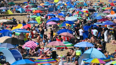 A Bournemouth beach full of people sitting under brightly-coloured sun umbrellas.