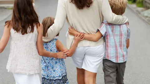 Getty Images Family of woman with three children walking along the road