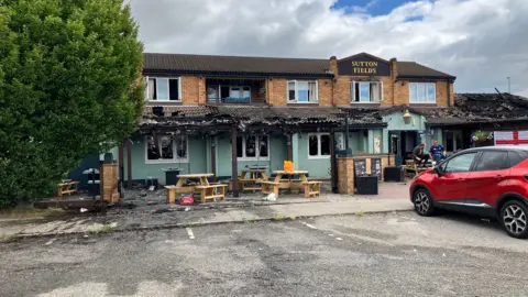 The 1970s style building has two floors, with a tiled wraparound porch around the first floor.  The tiles and porch are black and the tiles have been badly damaged.  The roof on an extension to the right of the building has been badly damaged.