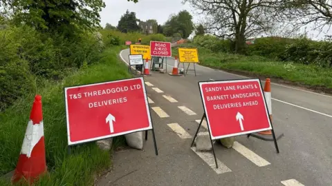 BBC/Ollie Conopo Road closure in rural area with red signs showing access for deliveries