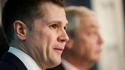 Robert Jenrick at a Reform UK press conference, with Nigel Farage in the background