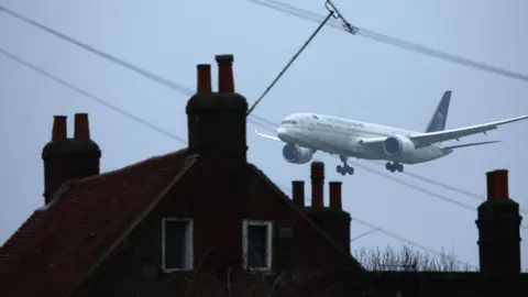 EPA A plane approaching Heathrow Airport, flying low over residential rooftops with chimneys and power lines visible.