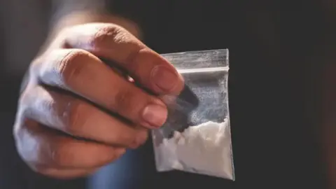 Getty Images A hand holding up a small transparent bag containing a white powder. 