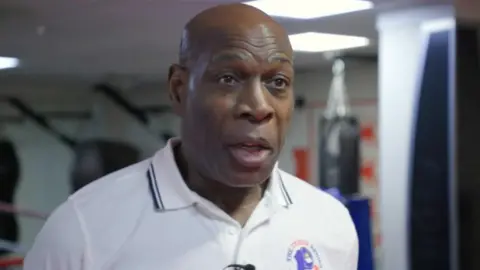 Frank Bruno is wearing a white polo shirt with his charitable foundation's logo on the front