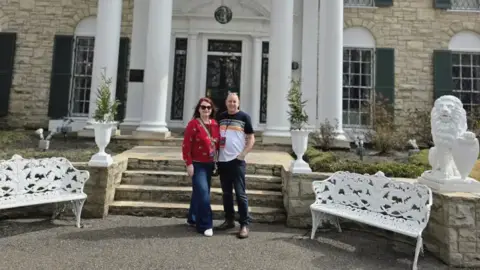 PA Real Life Man and woman smiling and standing next to each other in front of a large property.