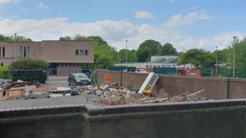 Rubbish including freezer on the car park with church and school behind.