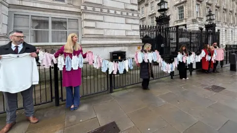 People stood outside Downing Street holding a long line of baby grows.