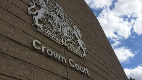 A close up view of the criminal courts crest and the words "crown court" on the Cambridge Crown Court building. It is a light coloured brick building. 