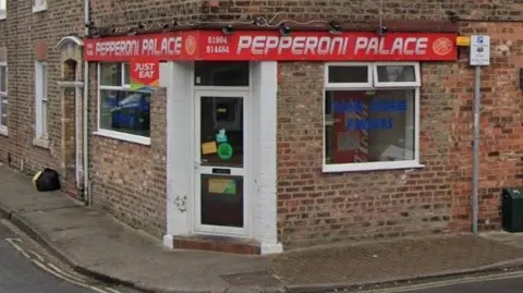 A white shop doorway at the junction of two terraced streets. Above the doorway is a red sign whith Pepperoni Palace written in white lettering.