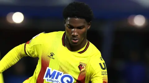 Vivaldo Semedo wearing a yellow and red Watford FC jersey during a match.