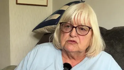 Jenny Sexton is wearing glasses and looking into the camera while being interviewed on a sofa 