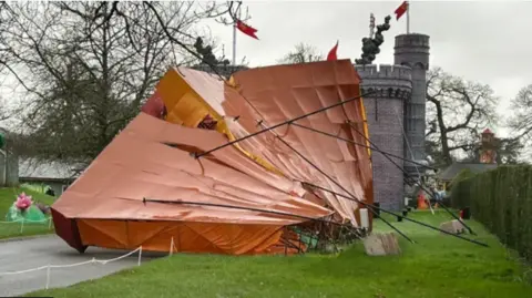 Longleat A large structure, which looks like a children's adventure play house at Longleat toppled on its side with a play castle in the background.