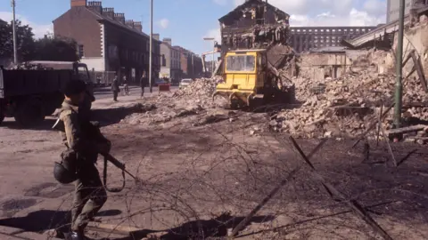 A soldier at a barbed wire barrier amid devastation in Falls Road, Belfast 