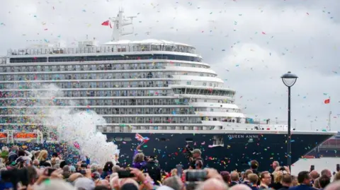 PA Media Cunard's Queen Anne is a large ship with a crowd of people cheering and confetti in the air